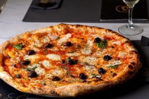 Wood-fired Margherita pizza with olives, served on a restaurant table with elegant tableware.
